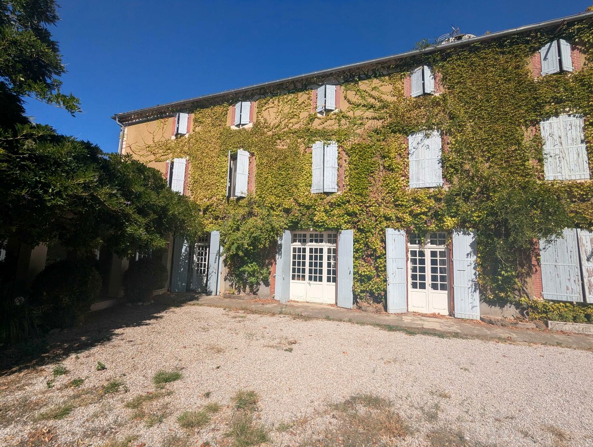La façade de la maison couverte de vigne vierge rousse en automne, entre les arbres du parc
