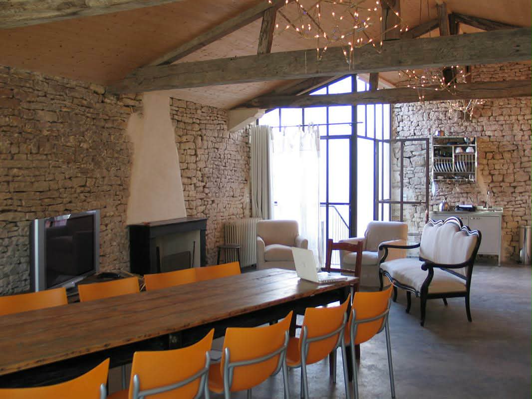 Grande salle conviviale du Domaine de La Planésié — table de travail en bois, espace salon attenant, pierres apparentes