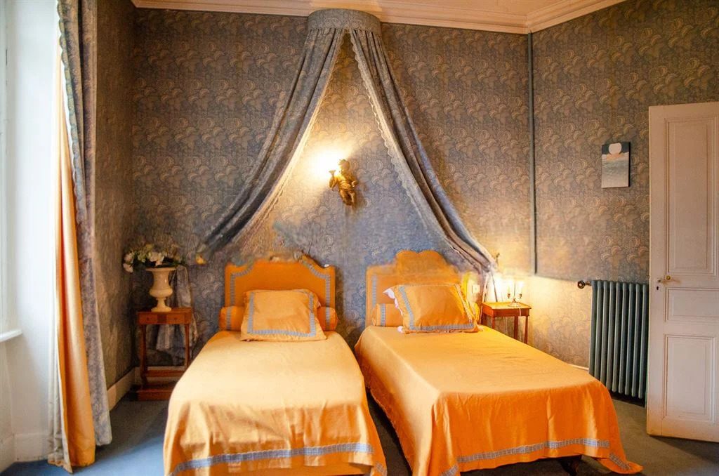 A twin bedroom with a draped bed canopy and blue patterned walls